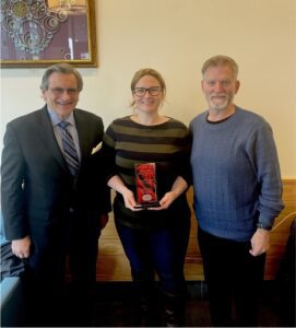 Three people standing in a room holding a plaque.