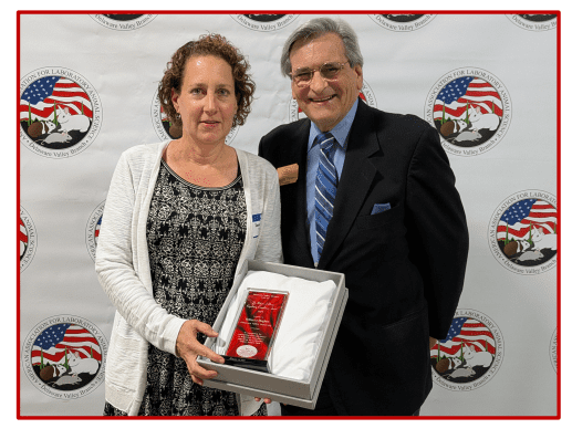 A woman and man pose with an award at an event.