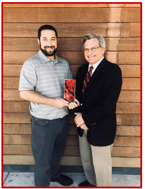 Two men smiling, holding a red award plaque together.