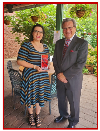 A smiling woman and man posing outdoors with a trophy.