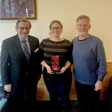 Three people standing in a room holding a plaque.