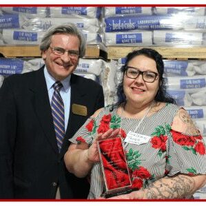 Two people smiling, woman holding award.