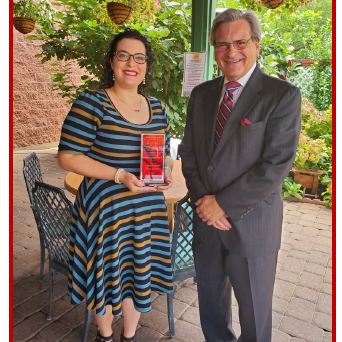 A smiling woman and man posing outdoors with a trophy.